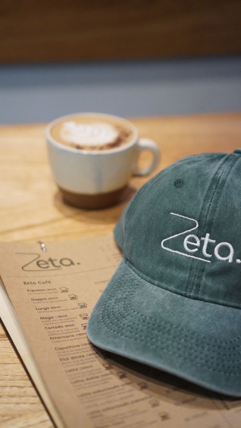 Capuchino junto a una gorra verde con el logo de Zeta y la carta del local
