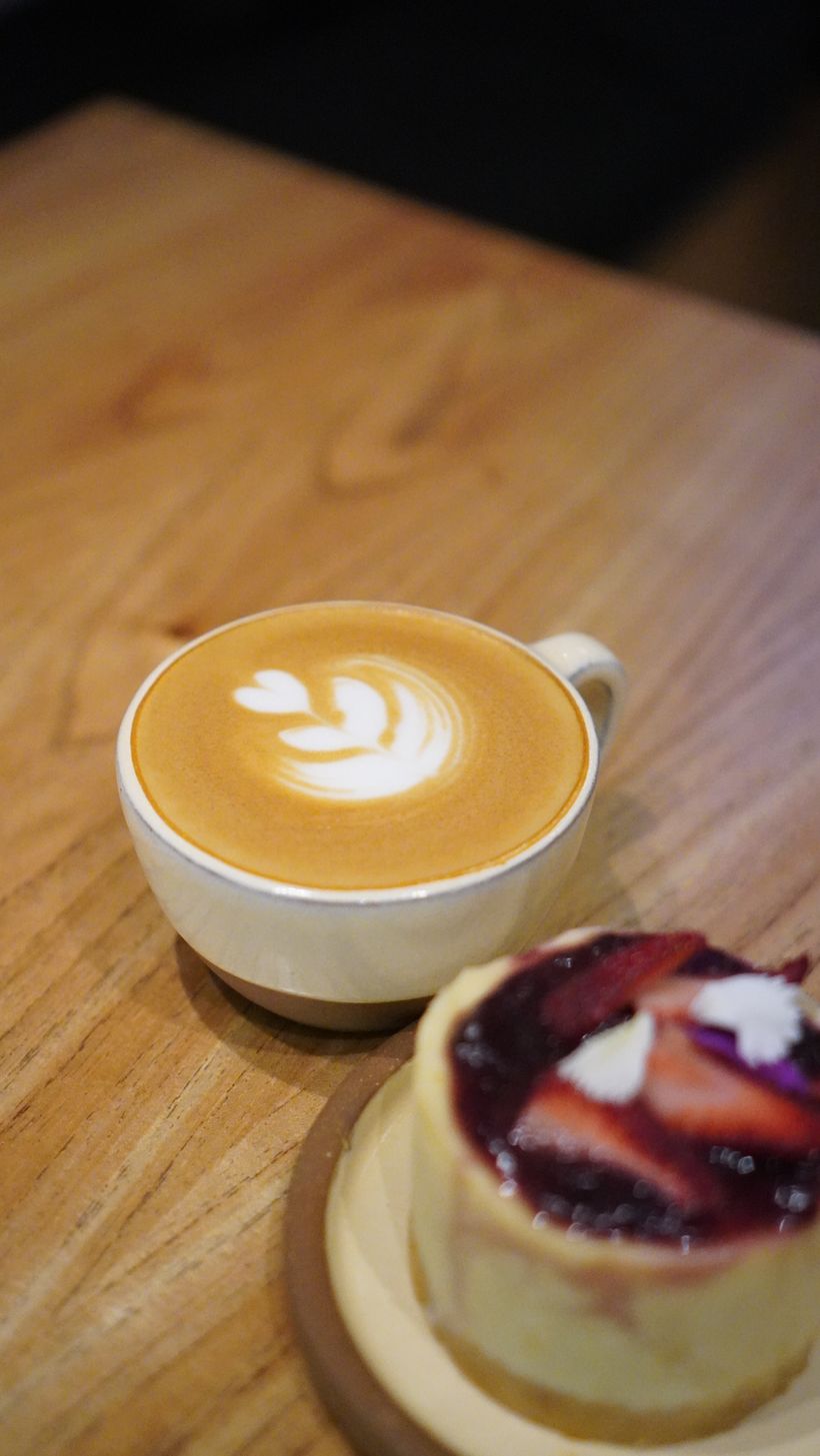 Flat white con arte latte y una porción de cheesecake de frutos rojos
