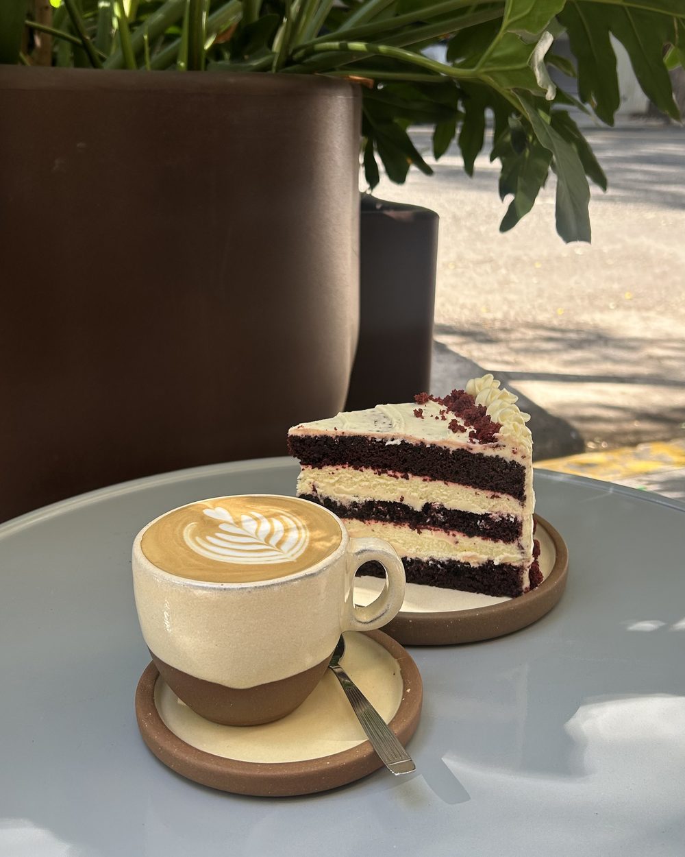 Flat white con arte latte junto a una porción de red velvet en la vereda de Zeta Café